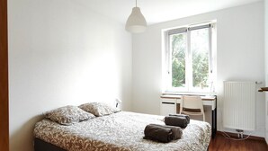A bedroom with a bed, a desk, and a window.