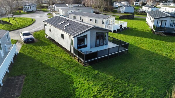 A modern mobile home with a large deck and a car parked in front.