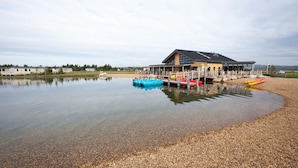 A lakeside building with a dock, kayaks, and a calm water body.