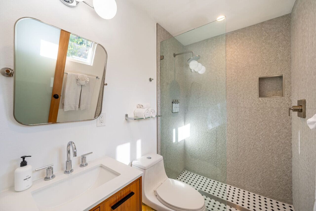 Een moderne badkamer met een grote spiegel, een douche met glazen wanden, een witte wastafel en een toilet.
