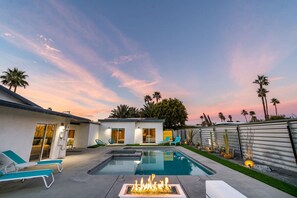 Una casa moderna con piscina, mobiliario exterior y una chimenea.