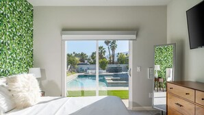 A bedroom with a bed, a dresser, a TV, and a sliding glass door leading to a pool area.