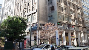 Um edifício de vários andares com fachada uniforme, diversas varandas e estacionamento com carros e motocicletas.