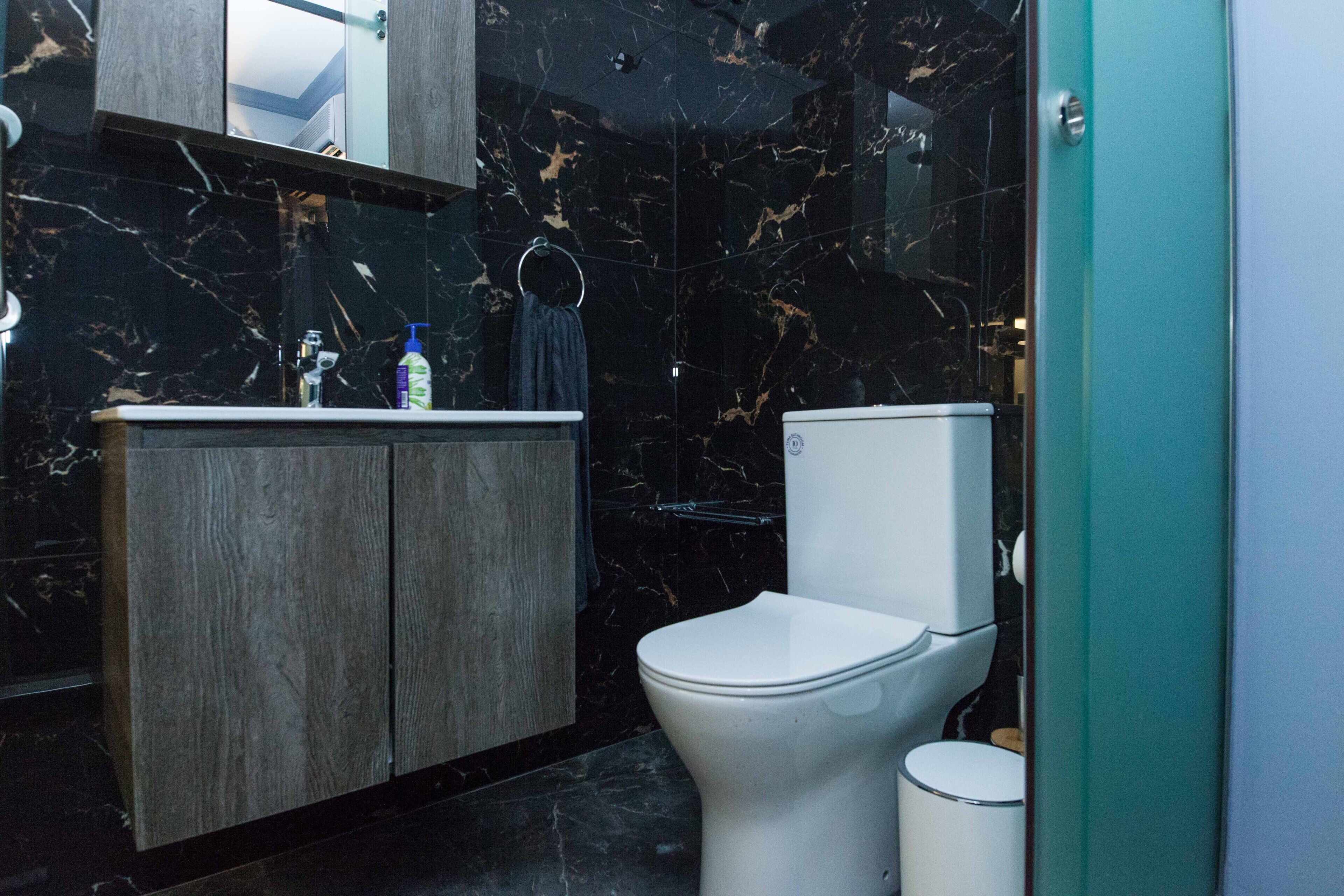 A modern bathroom with a marble backsplash, a wooden vanity, a white toilet, and a glass shower enclosure.