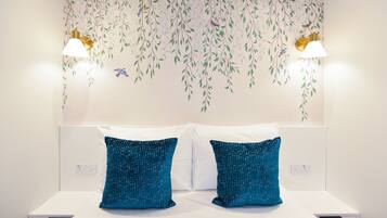 A hotel room with a bed, two blue patterned pillows, a white headboard, and wall-mounted lamps.