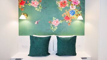 Une chambre à coucher avec un mur décoré d’un motif floral vert, deux coussins verts et des lampes de chevet.