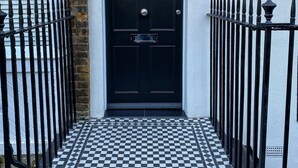 A black door with the number 21, a checkered tile floor, and a black iron fence. - Sale Place Serviced Apartments by Concept Apartments (London)