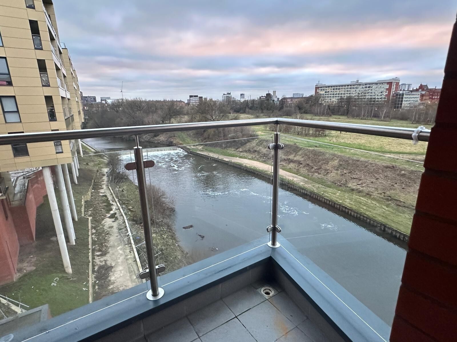 A balcony with a view of a river, buildings, and a cloudy sky.