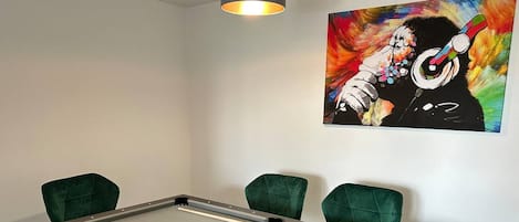 A pool table with four green chairs, a painting on the wall, and a ceiling light.