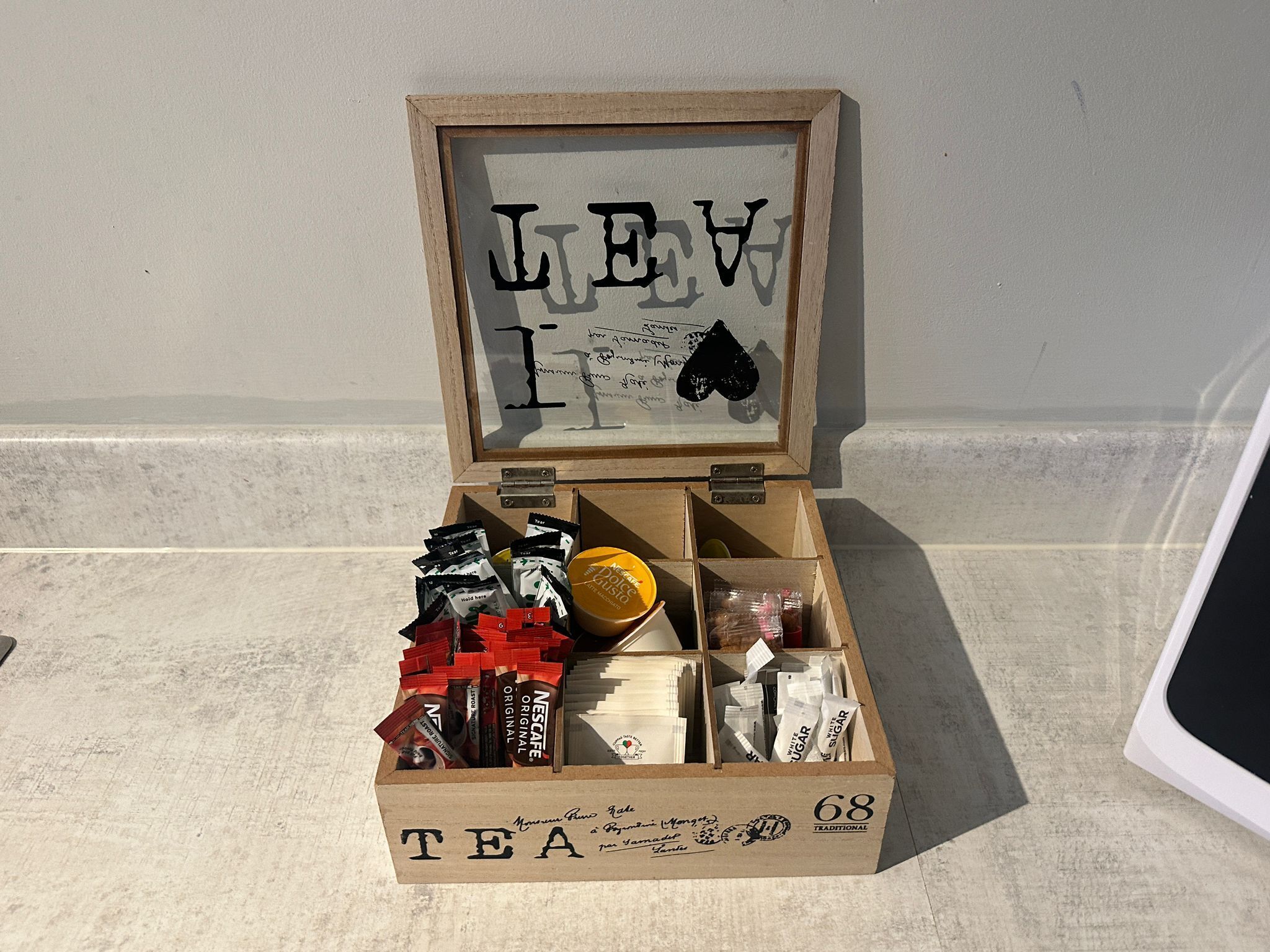 Une boîte en bois étiquetée « THÉ », comportant des compartiments contenant différents types de thé, et une plaque encadrée portant l’inscription « LEV I ».