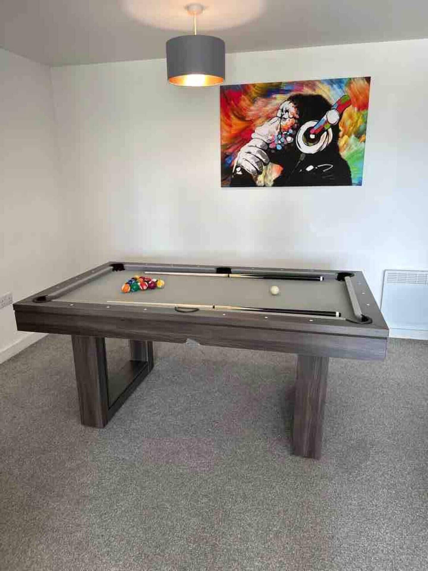 Ein Billardtisch mit Kugeln, ein farbenfrohes Bild an der Wand und eine hängende Leuchte.