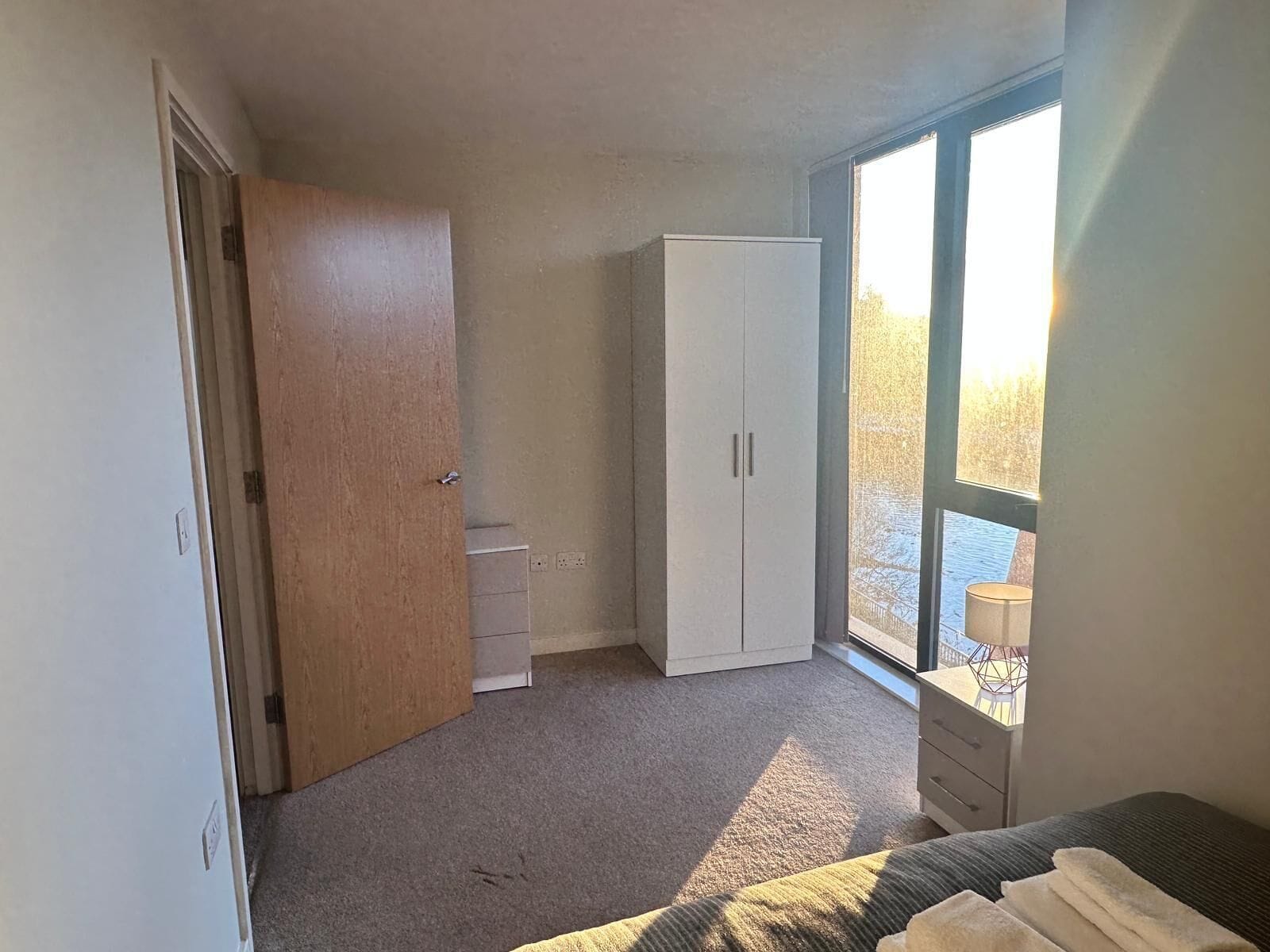 A bedroom with a large window, a wardrobe, a bed, and a small desk.