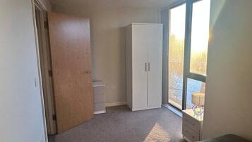 A bedroom with a large window, a wardrobe, a bed, and a small desk.