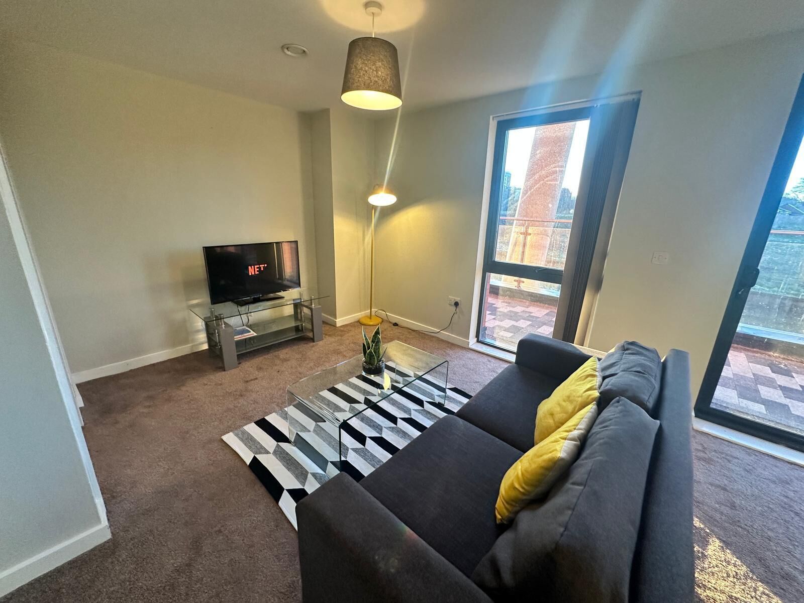 A modern living room with a sofa, a TV, a lamp, and a large window.