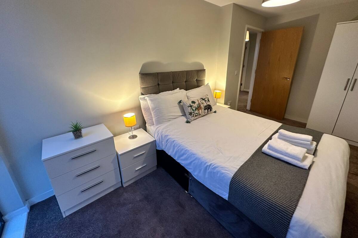 Une chambre à coucher comprenant un lit, des tables de chevet, une commode, une lampe, une armoire et une porte.