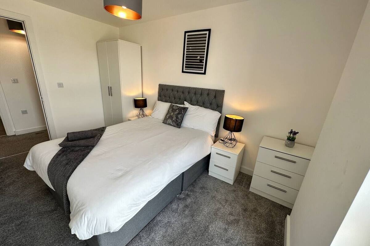 Une chambre à coucher moderne avec un grand lit, deux tables de chevet, une armoire et un luminaire fixé au plafond.