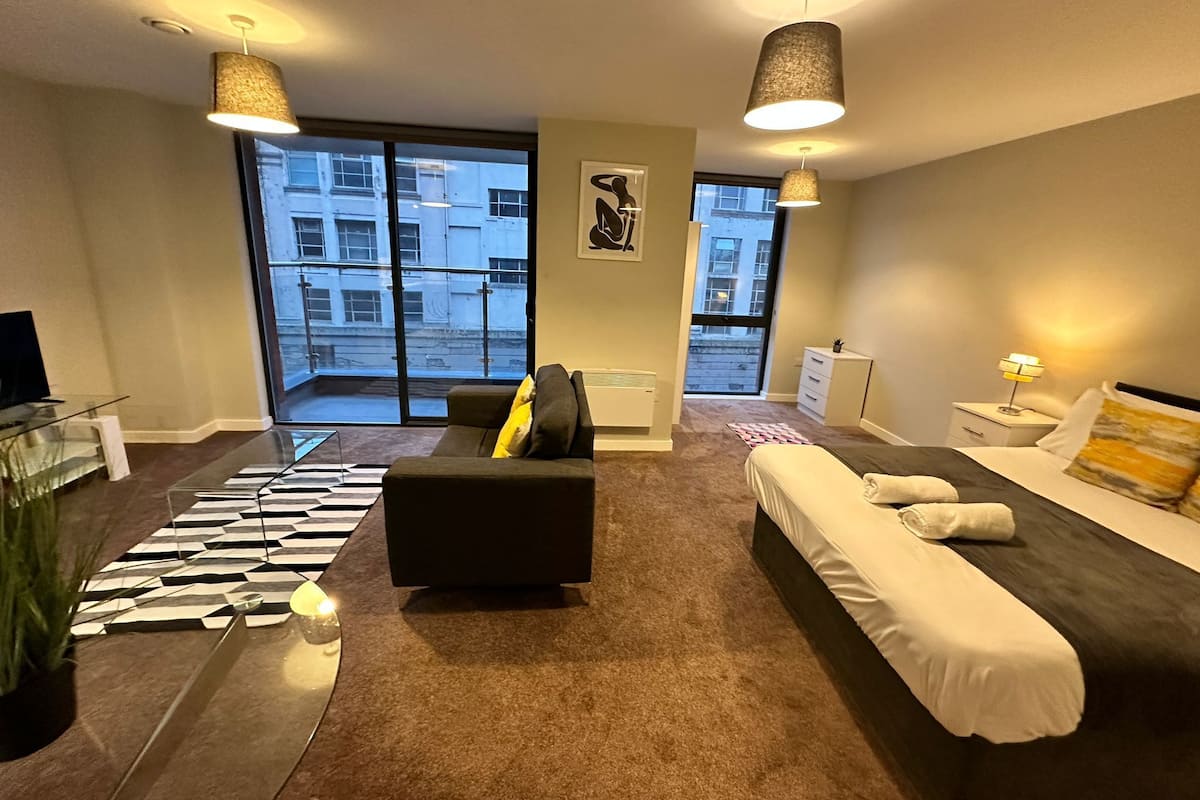 Une chambre d’hôtel moderne, dotée d’un canapé, d’un lit, d’une table basse en verre et offrant une vue sur la ville grâce à de grandes fenêtres.