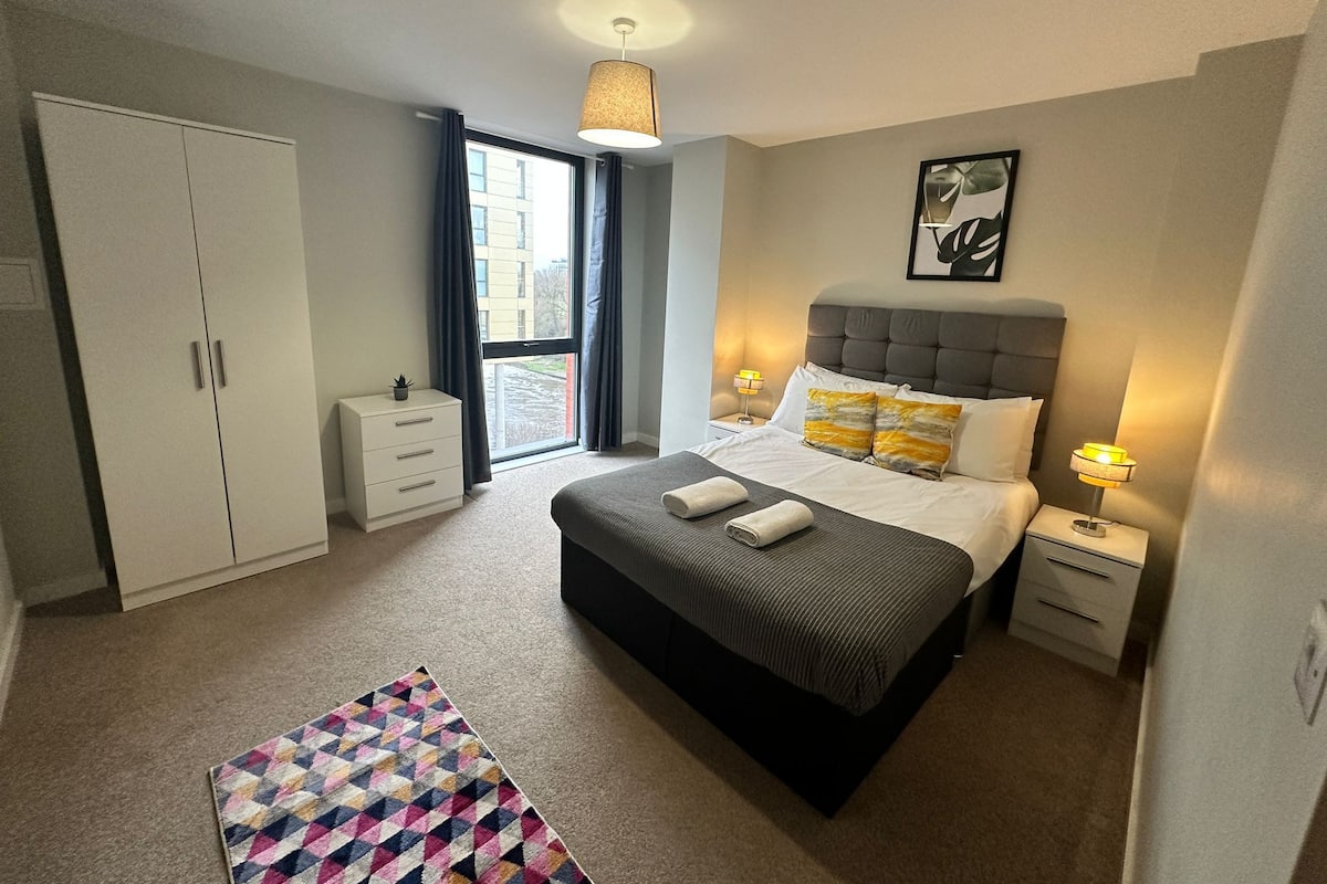 Une chambre moderne avec un grand lit, des tables de chevet, une armoire et une vue sur l’extérieur.