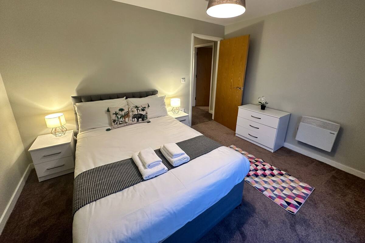 Une chambre bien rangée, avec un grand lit, des tables de chevet, une commode et un radiateur.