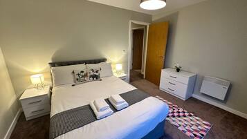 A neatly arranged bedroom with a large bed, bedside tables, a dresser, and a radiator.