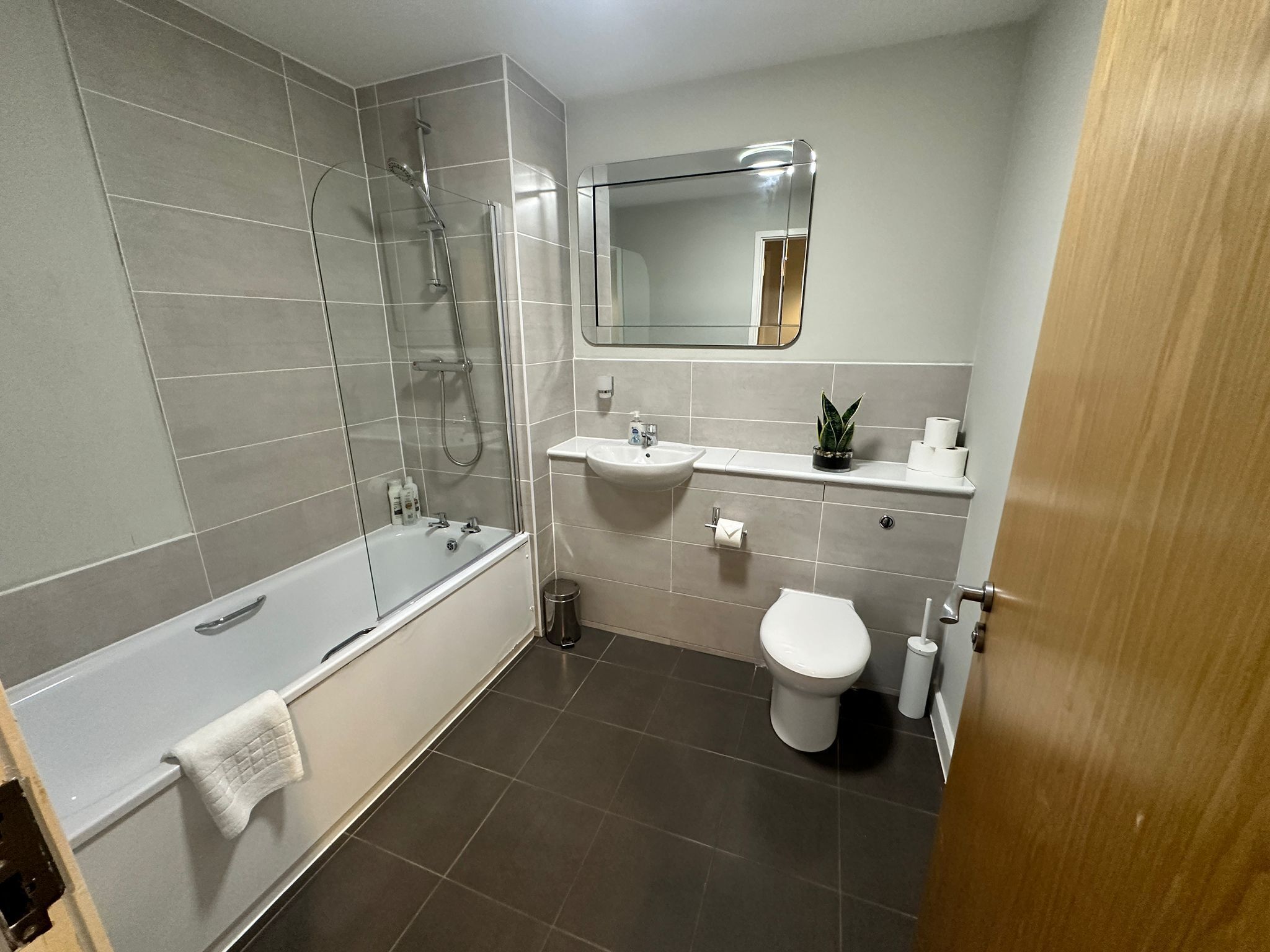 A modern bathroom with a glass-enclosed shower, a white bathtub, a sink, and a toilet.