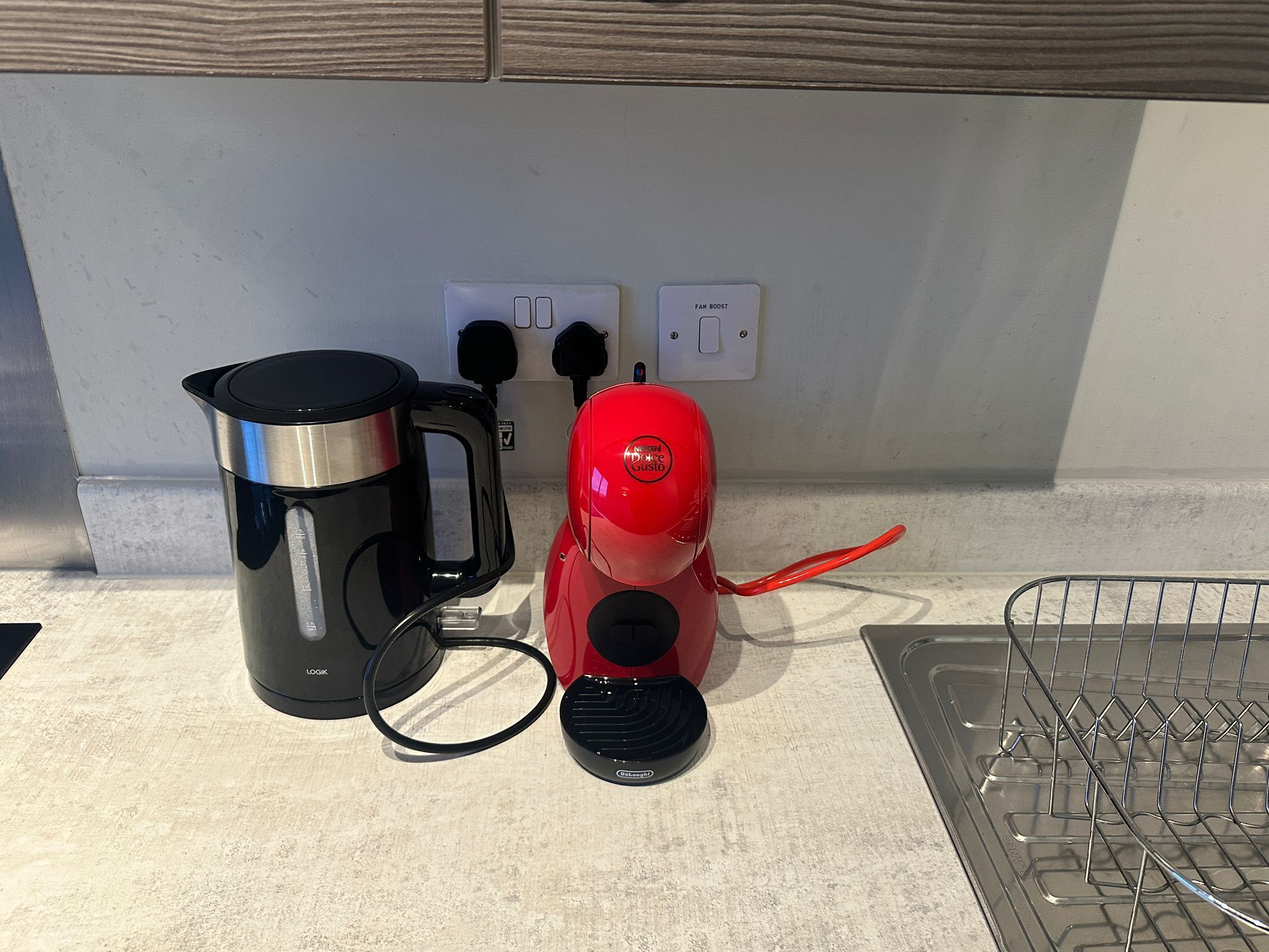 A kitchen counter with a black coffee maker, a red electric kettle, and a power outlet with a switch.