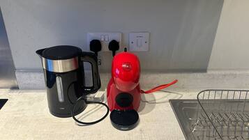 Un piano di lavoro in cucina con una macchina da caffè nera, un bollitore elettrico rosso e una presa di corrente con interruttore.