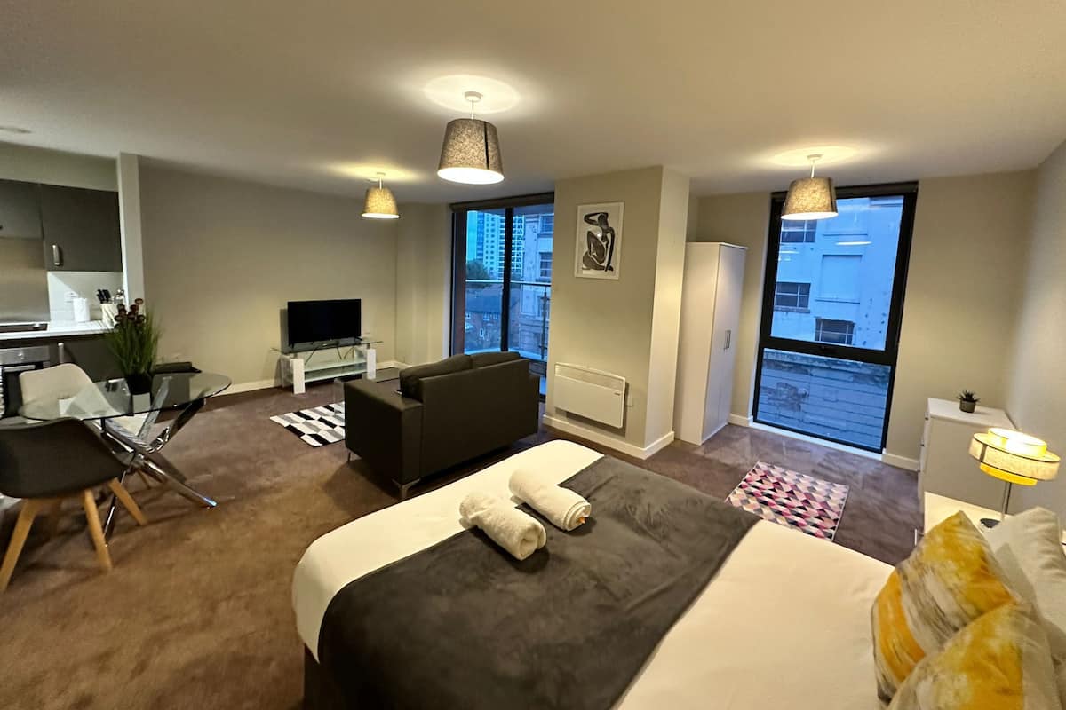 Une chambre d’hôtel moderne équipée d’un lit, d’un canapé, d’une télévision, d’un coin repas et de grandes fenêtres.