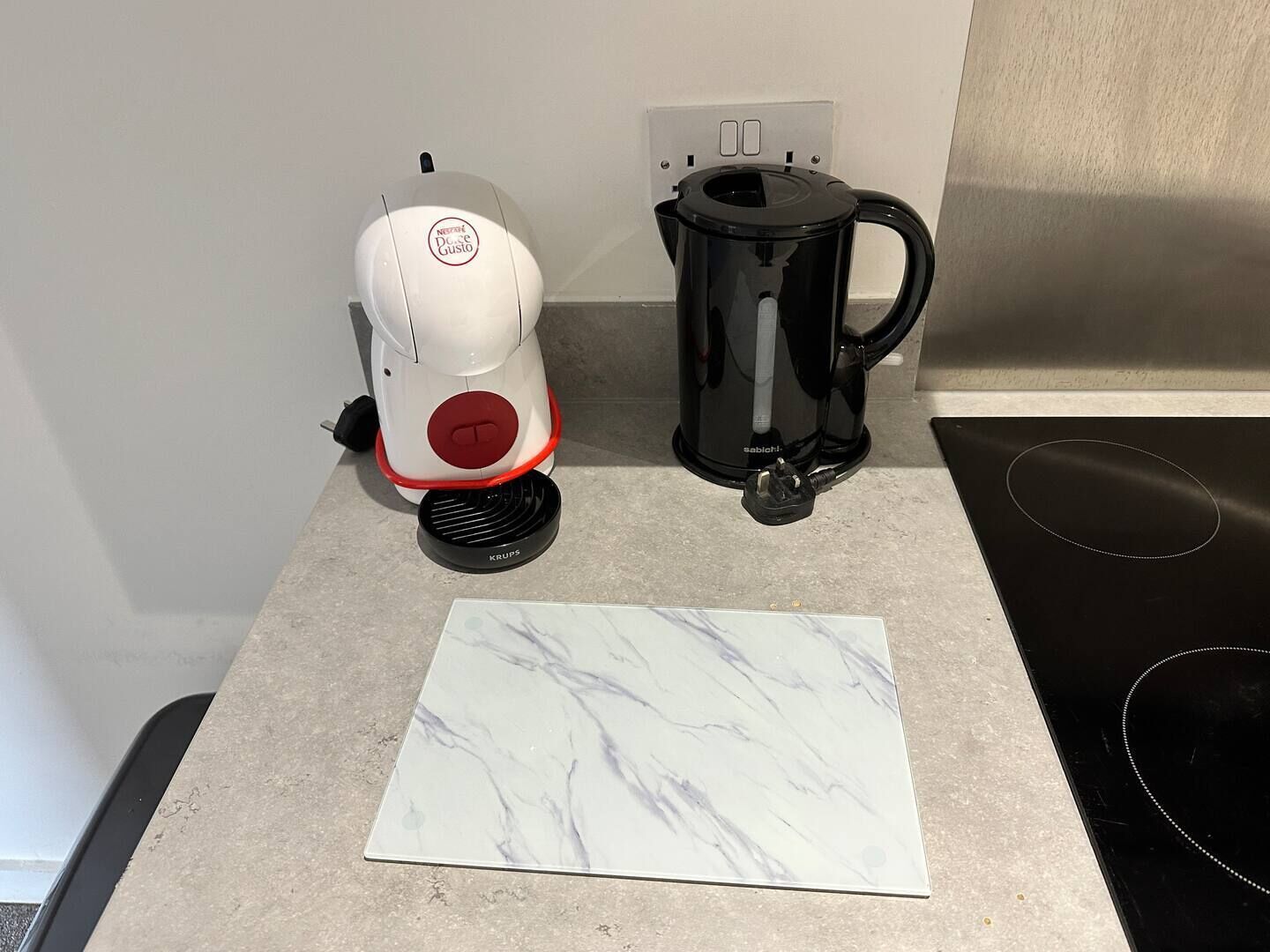 Una encimera de cocina con una cafetera blanca, una jarra de café negra y baldosas de mármol.