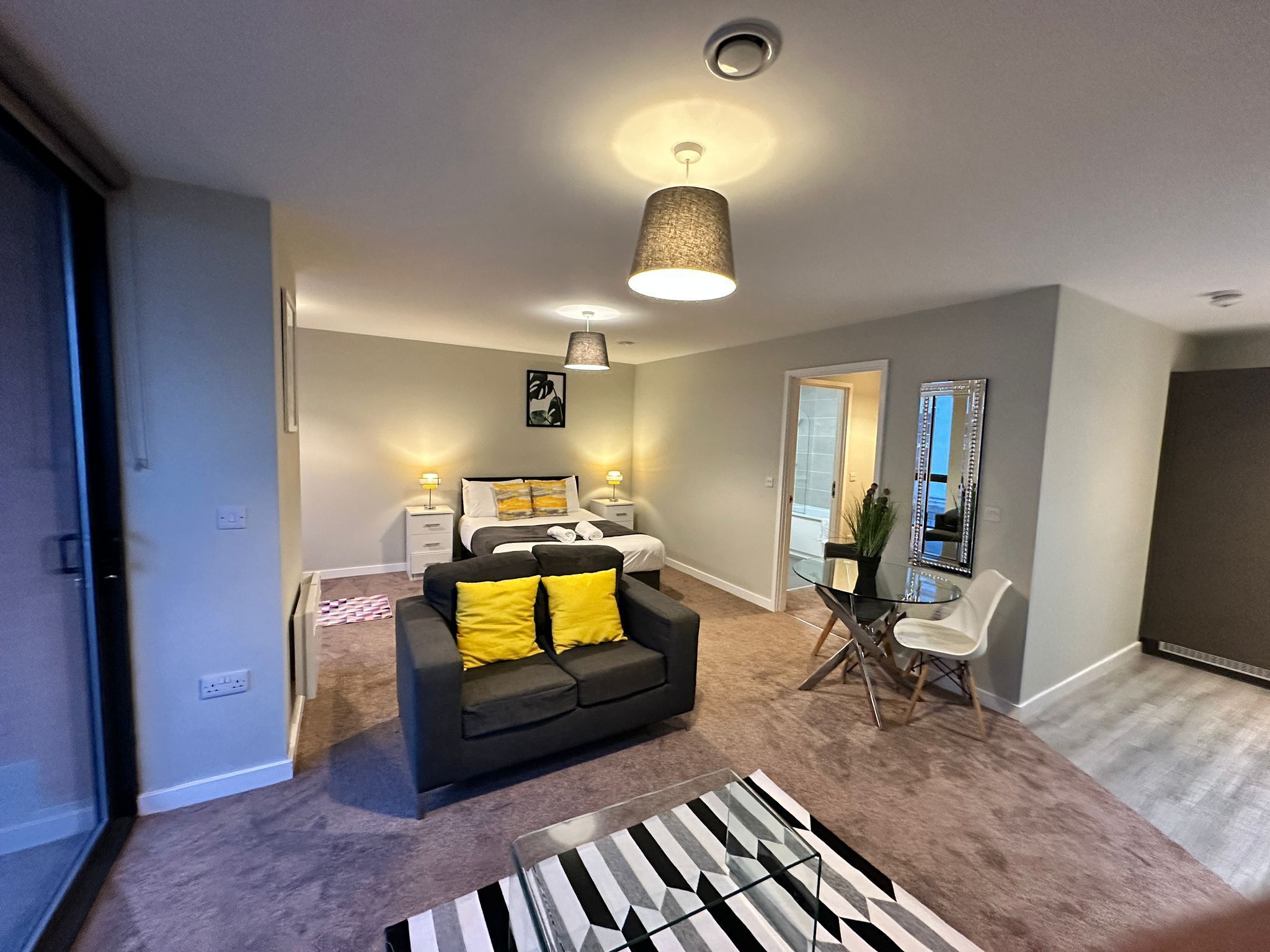 A modern living room with a sofa, a glass coffee table, and a dining area with a chair and table.