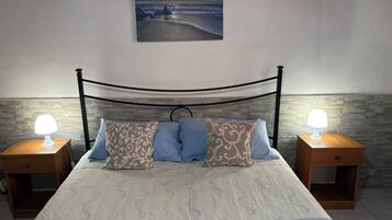 Ein Bett mit Kopfteil, zwei Nachttische mit Lampen, gemusterte Kissen und ein Bild an der Wand.