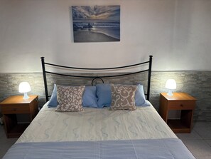 A bed with a headboard, two bedside tables with lamps, patterned pillows, and a painting on the wall.