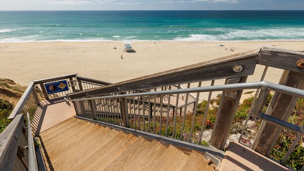 A wooden staircase leading to a beach with a lifeguard tower and a clear view of the ocean.