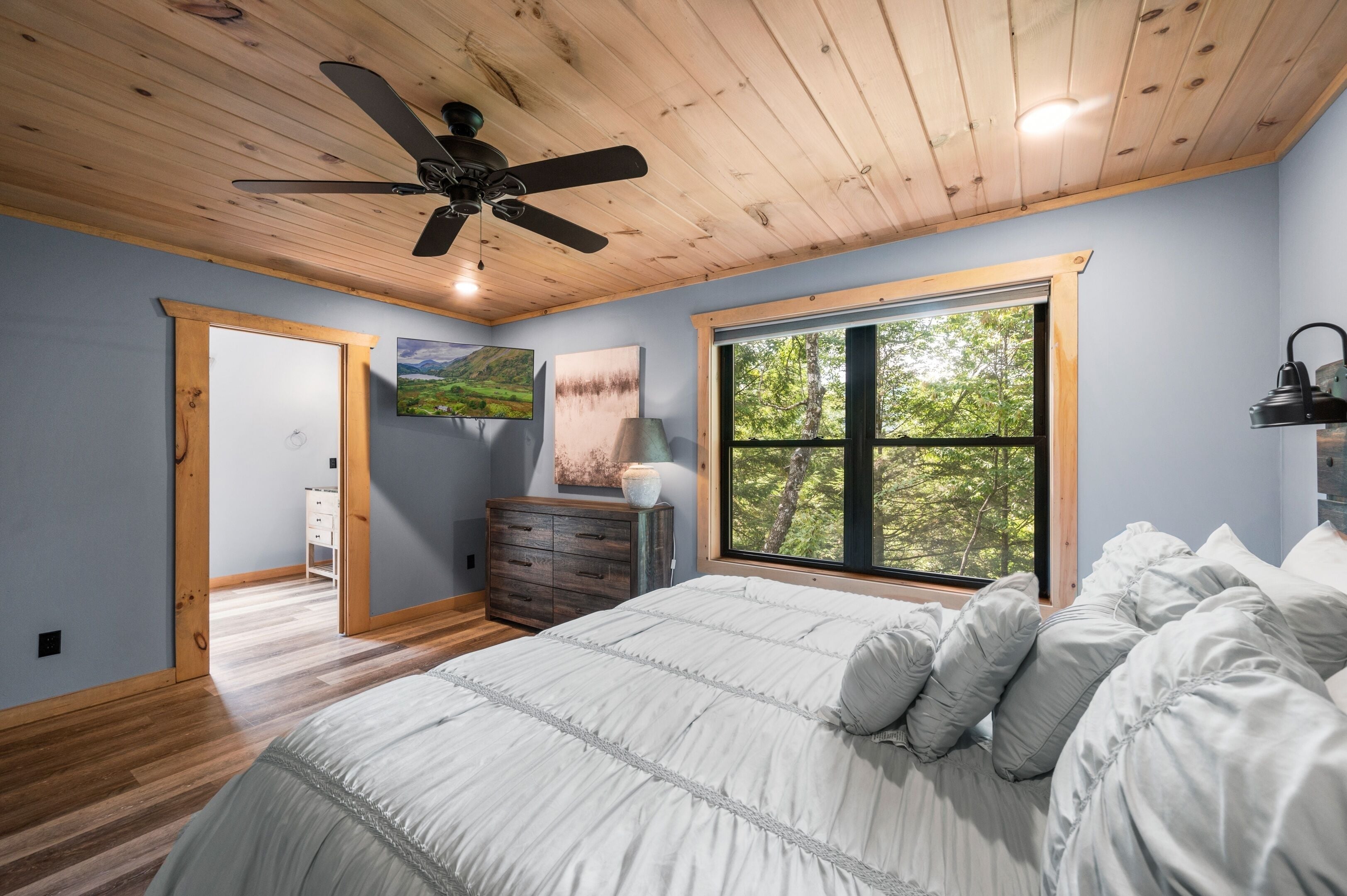 Ein Schlafzimmer mit einem großen Bett, Holzboden und einem Fenster mit Blick auf Bäume.