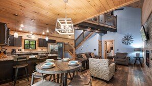 A spacious kitchen with wooden cabinets, a dining area with a round table, and a living room with a fireplace. - Haven 2 Bedroom Cabin by RedAwning (Gatlinburg)
