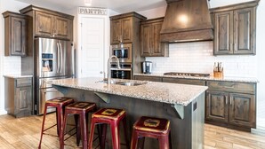 A modern kitchen with dark wood cabinets, stainless steel appliances, a granite island, and red bar stools. - Zion Experience 4 Bedroom Townhouse by RedAwning (Washington)