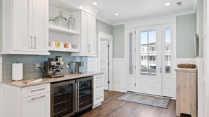 A modern kitchen with white cabinetry, a coffee station, and a view of the outside. - Fish-n-chips By The Sea 6 Bedroom Home by RedAwning (Supply)