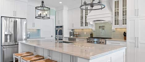 A modern kitchen with white cabinetry, stainless steel appliances, a large island with bar stools, and pendant lighting.