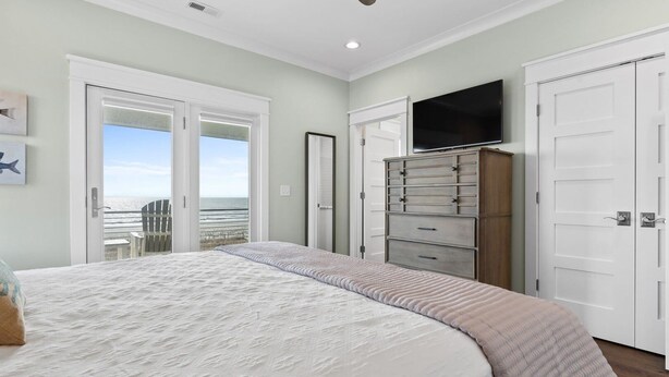 A bedroom with a large bed, a dresser, a TV, and a view of the beach through a door. - Fish-n-chips By The Sea 6 Bedroom Home by RedAwning (Supply)