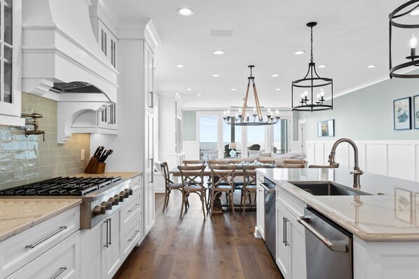 A modern kitchen with white cabinetry, a central island, and a dining area with wooden chairs.