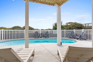 A pool area with a covered seating area, lounge chairs, and a white picket fence.