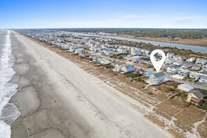 A coastal residential area with houses along the beach, a river in the background, and a clear sky.