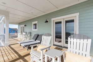 Terraza techada al aire libre con sillones de descanso y una mesa, con vista a una playa.