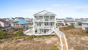 A multi-story beachfront house with a wooden deck and a staircase leading to the upper level. - Fish-n-chips By The Sea 6 Bedroom Home by RedAwning (Supply)