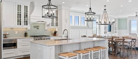 A spacious kitchen with white cabinetry, a central island with stools, pendant lighting, and a view to the dining area.