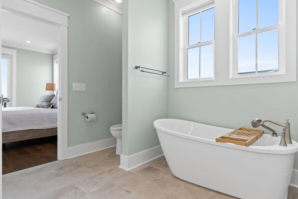 A bathroom with a freestanding bathtub, a window, and a toilet.
