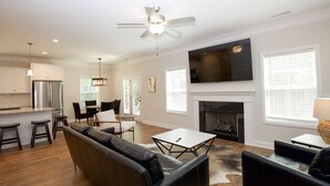 A modern living room with a fireplace, a large TV, and a dining area with a chandelier. - Great Location! 4 Bed / 4.5 Bath House in Pinehurst! (Pinehurst)