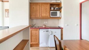 A compact kitchen with wooden cabinets, a microwave, and a dishwasher. - Résidence Le Rami Les Coches - La Plagne (La Plagne-Tarentaise)