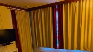 A hotel room with a wooden coffee table, a TV on the left, and a window with yellow curtains. - Résidence Le Rami Les Coches - La Plagne (La Plagne-Tarentaise)