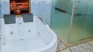 Un baño con una bañera grande, cabina de ducha de vidrio y ventana con vistas a un edificio rojo.